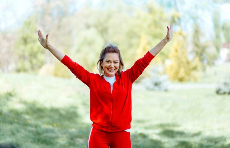 Femme souriante dans un parc, bras levés en signe de joie et de bien-être